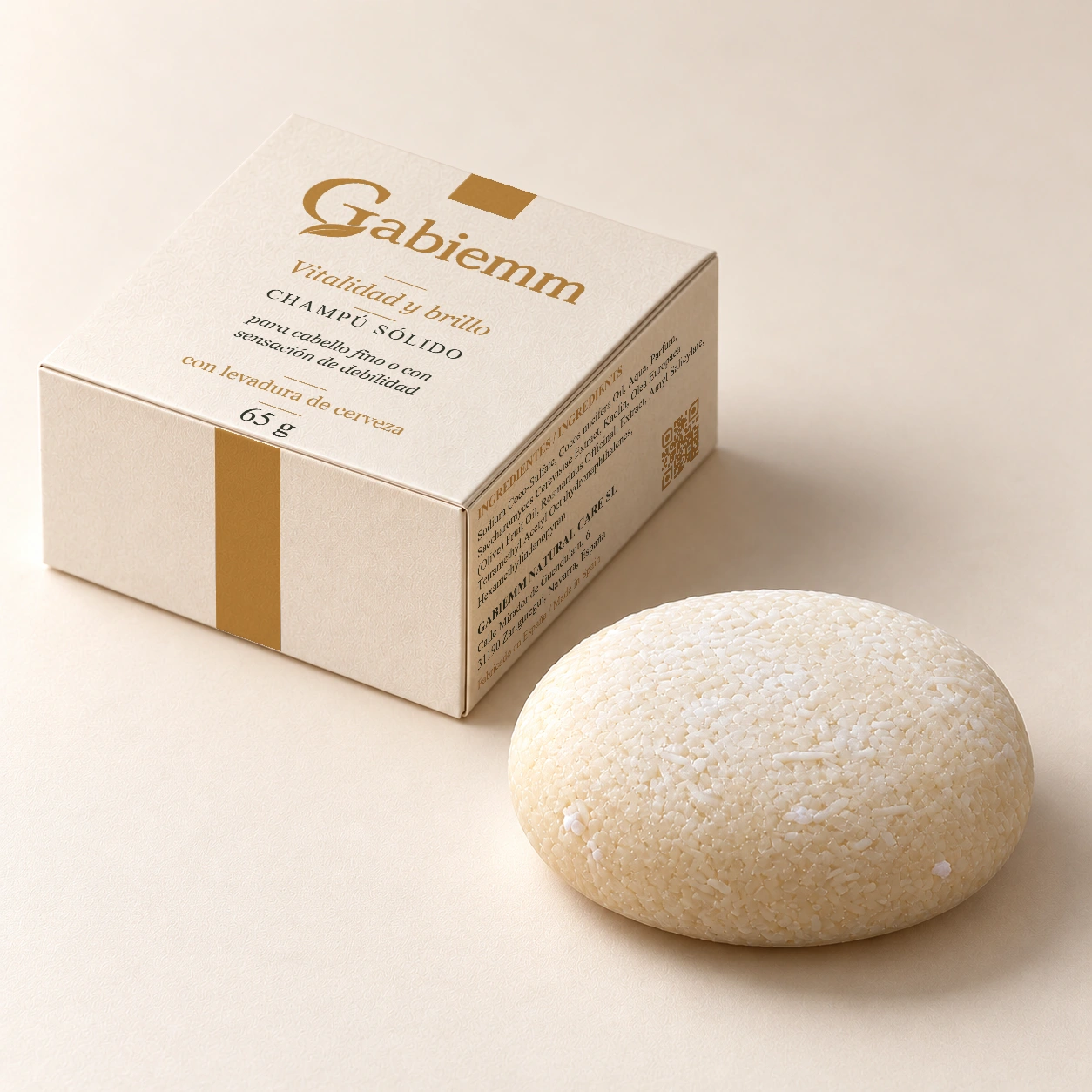 Mockup digital de la caja Vitalidad y brillo de Gabiemm, de 65 g, junto a su pastilla de champú sólido. Se conserva el diseño original de tapa y caras visibles; pastilla de forma abombada y bordes redondeados.